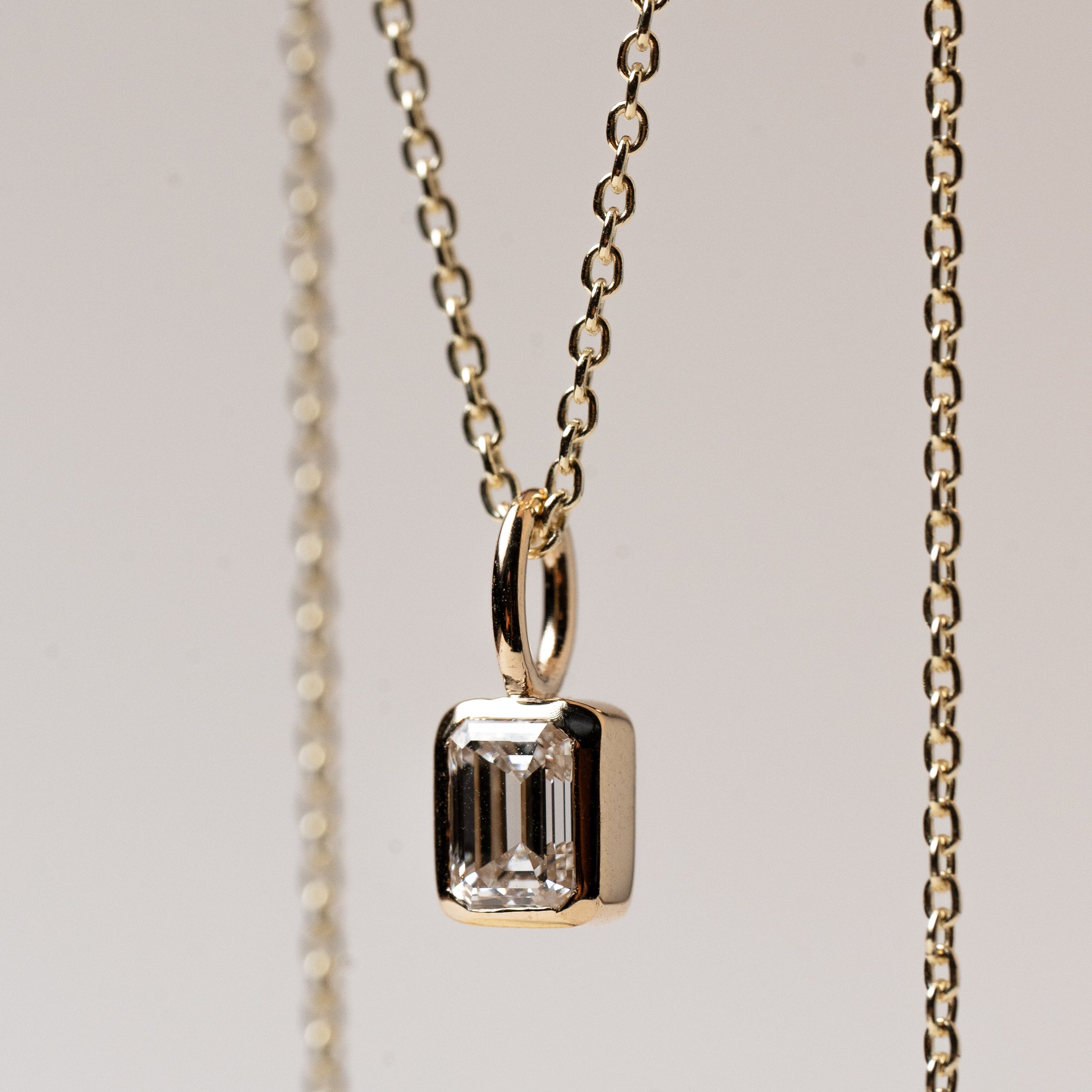 Gold necklace with emerald cut diamond pendant on a light background