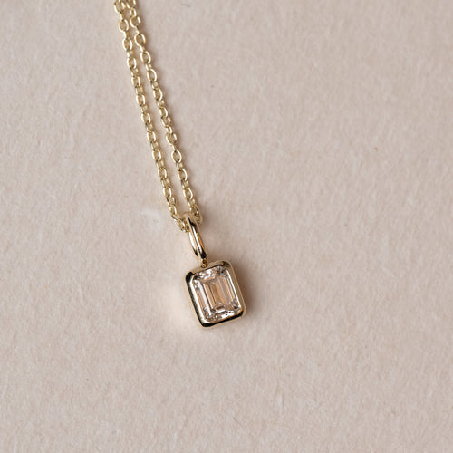 Necklace with a emerald cut diamond pendant on a beige background
