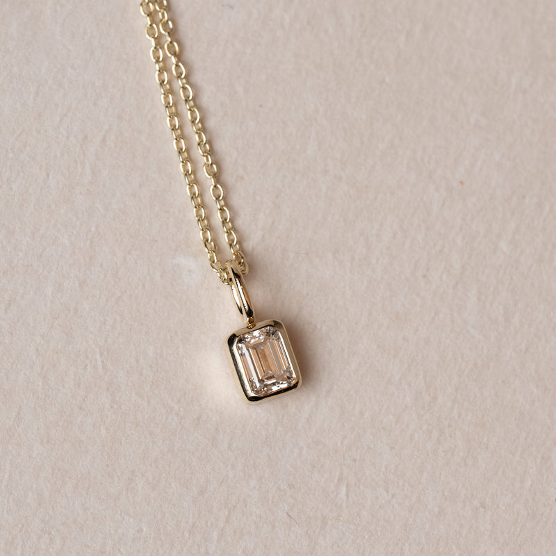 Necklace with a emerald cut diamond pendant on a beige background