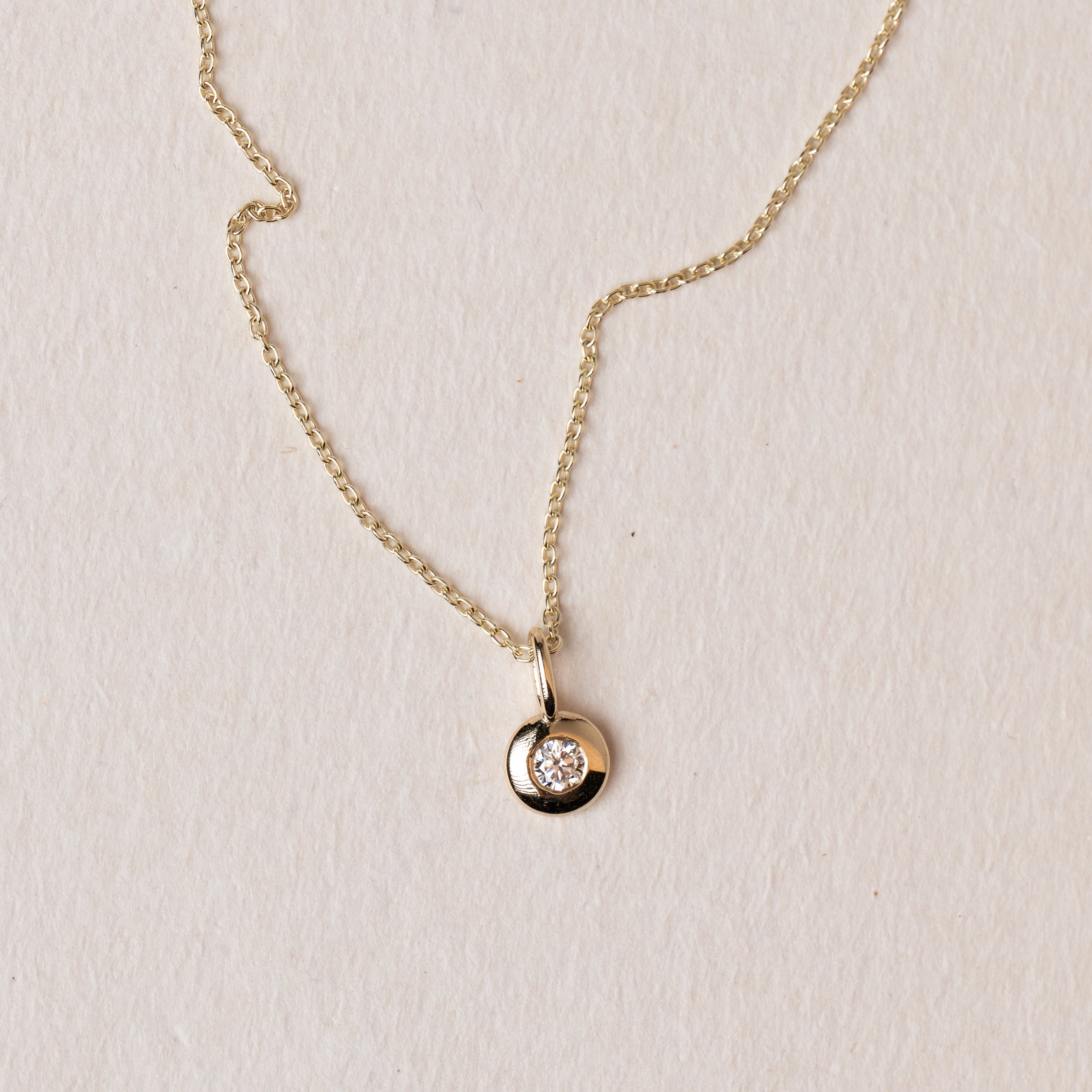 Gold necklace with a small round diamond pendant on a light beige background
