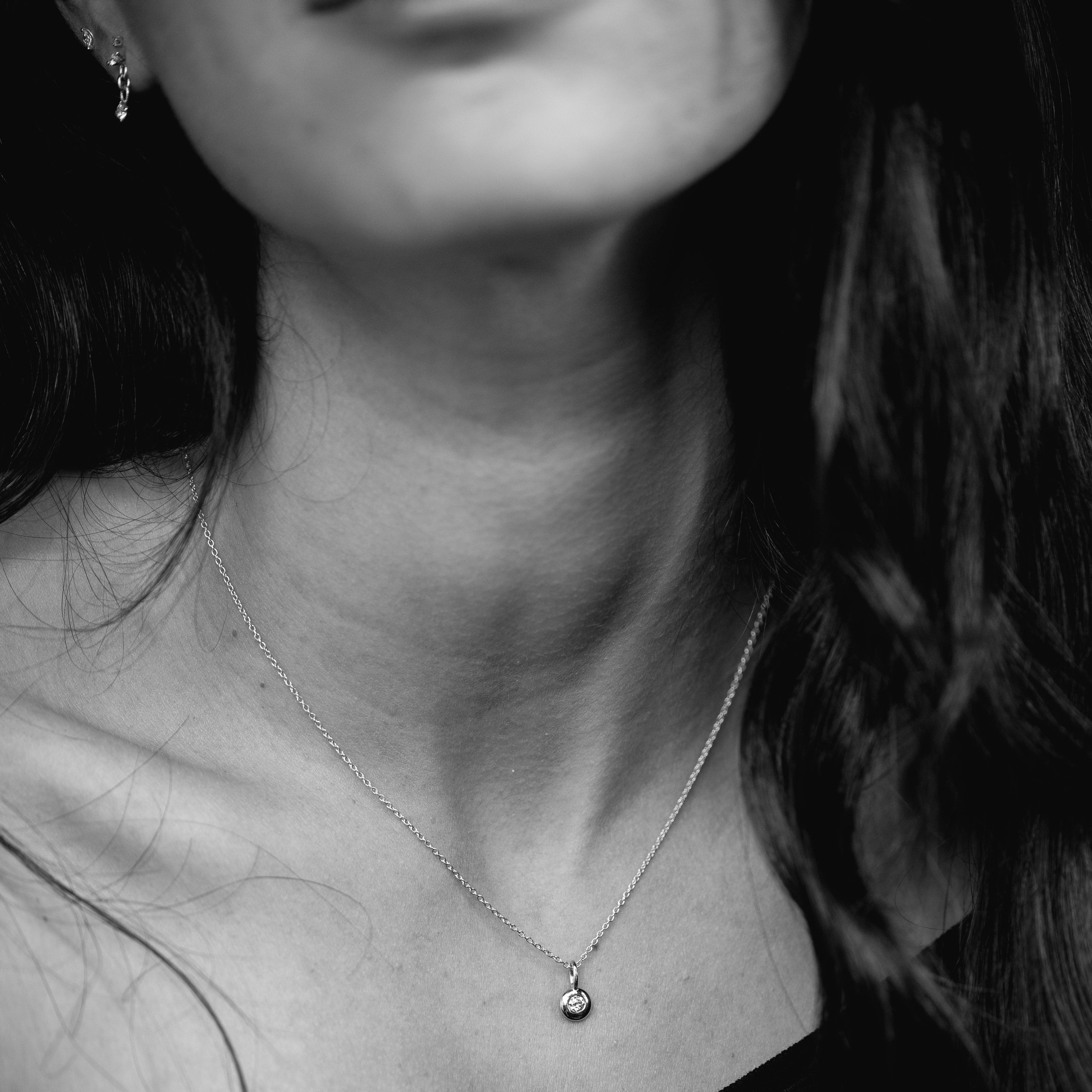 Close-up of a person wearing a necklace with a diamond pendant.