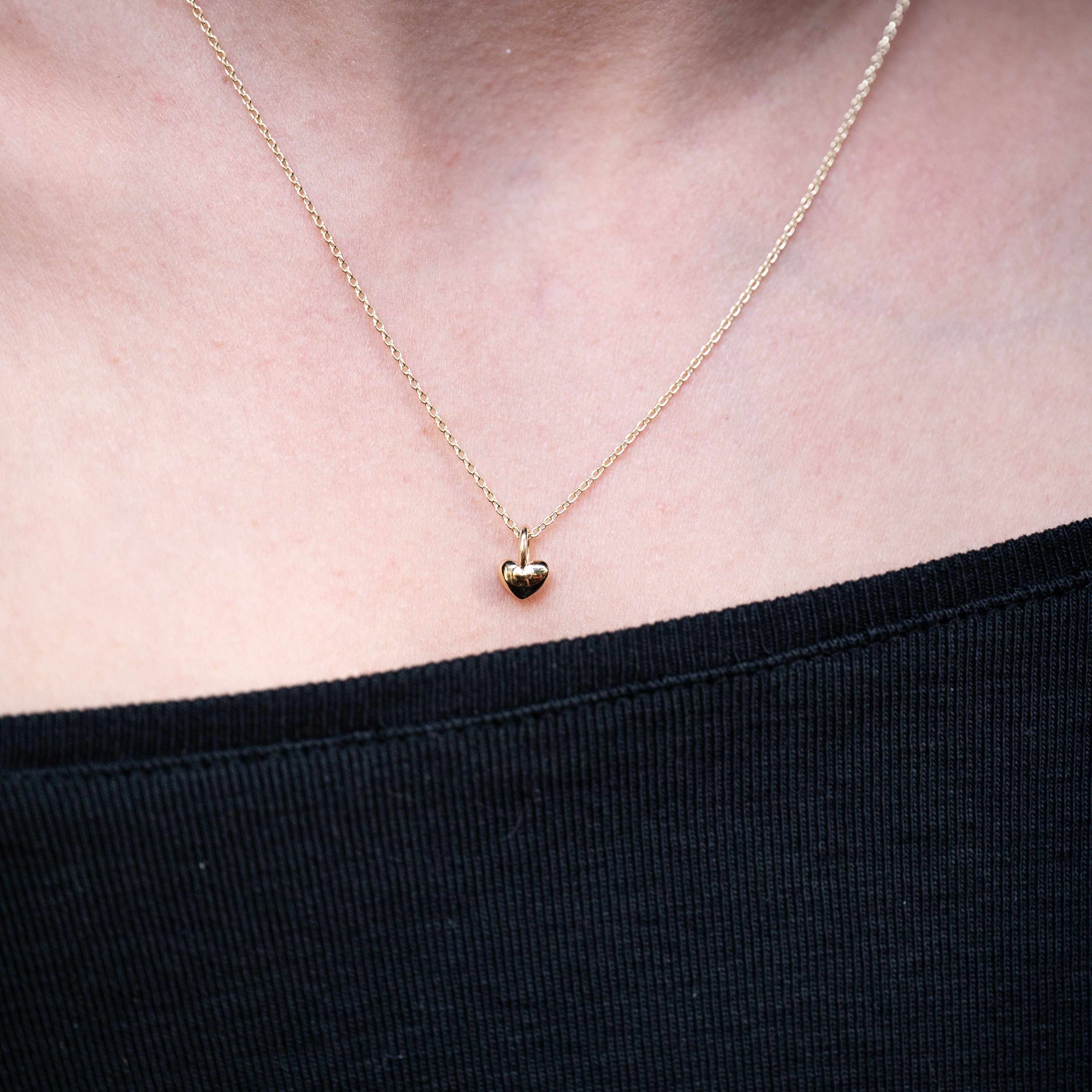Gold necklace with a heart pendant on a person wearing a black top.