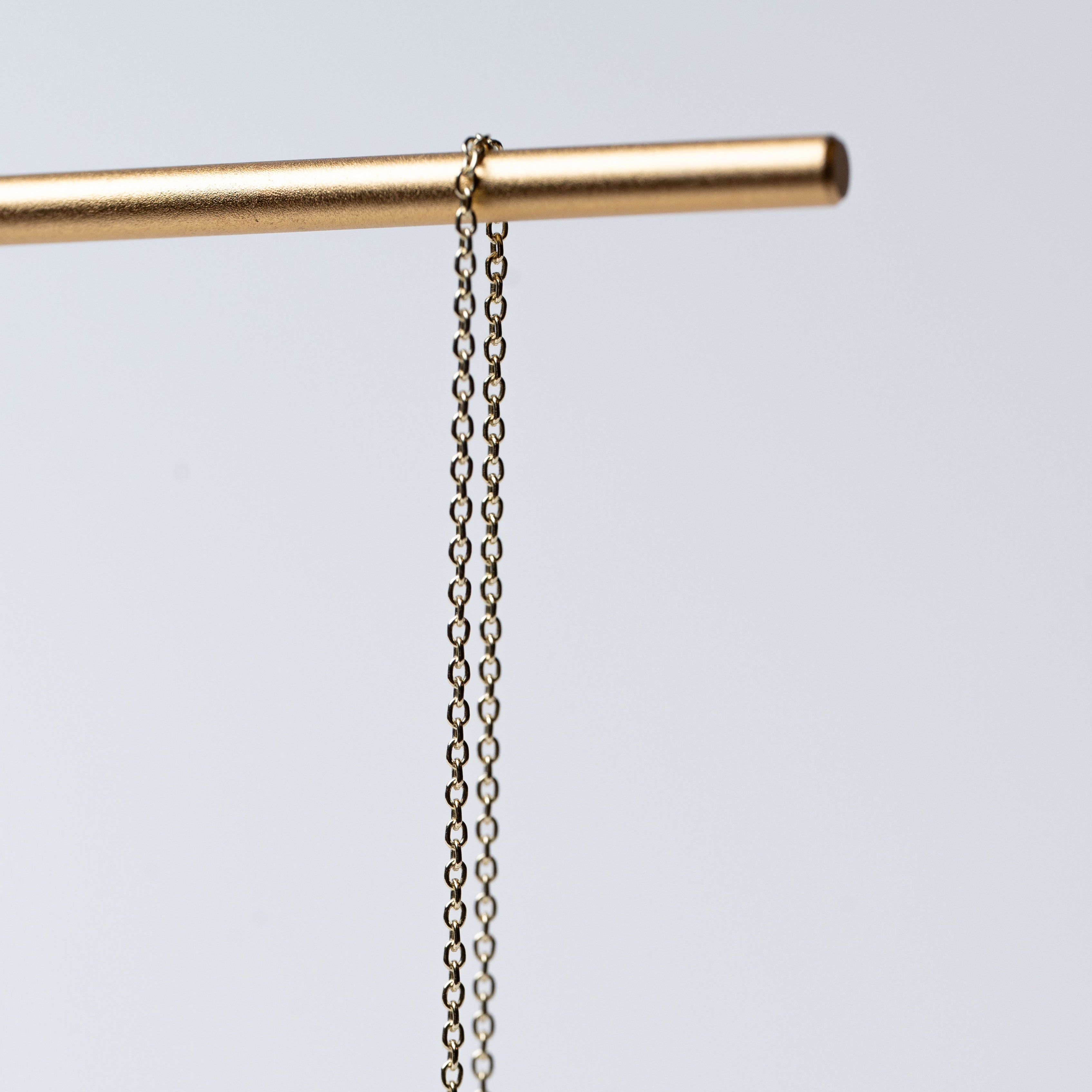 Gold bar with a chain hanging from it on a light gray background