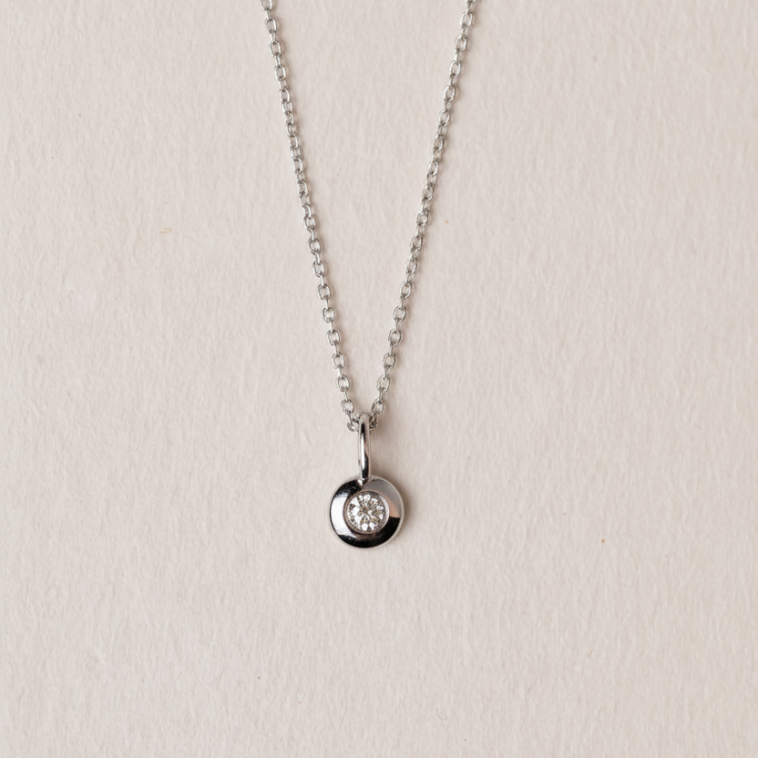 White gold necklace with a round pendant on a light beige background